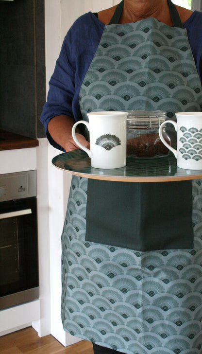 Bild med person och förkläde, muggar och bricka