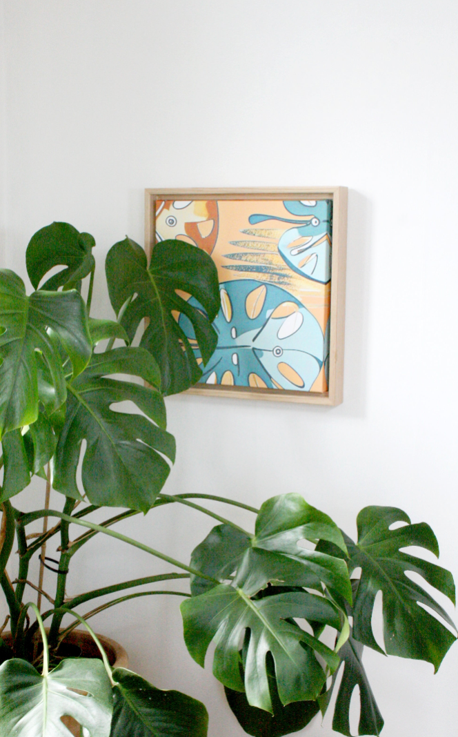 Monstera väggkonst nordisk tavla 30×30 - inramad tavla på vit vägg bredvid gröna monstera-växter i hem