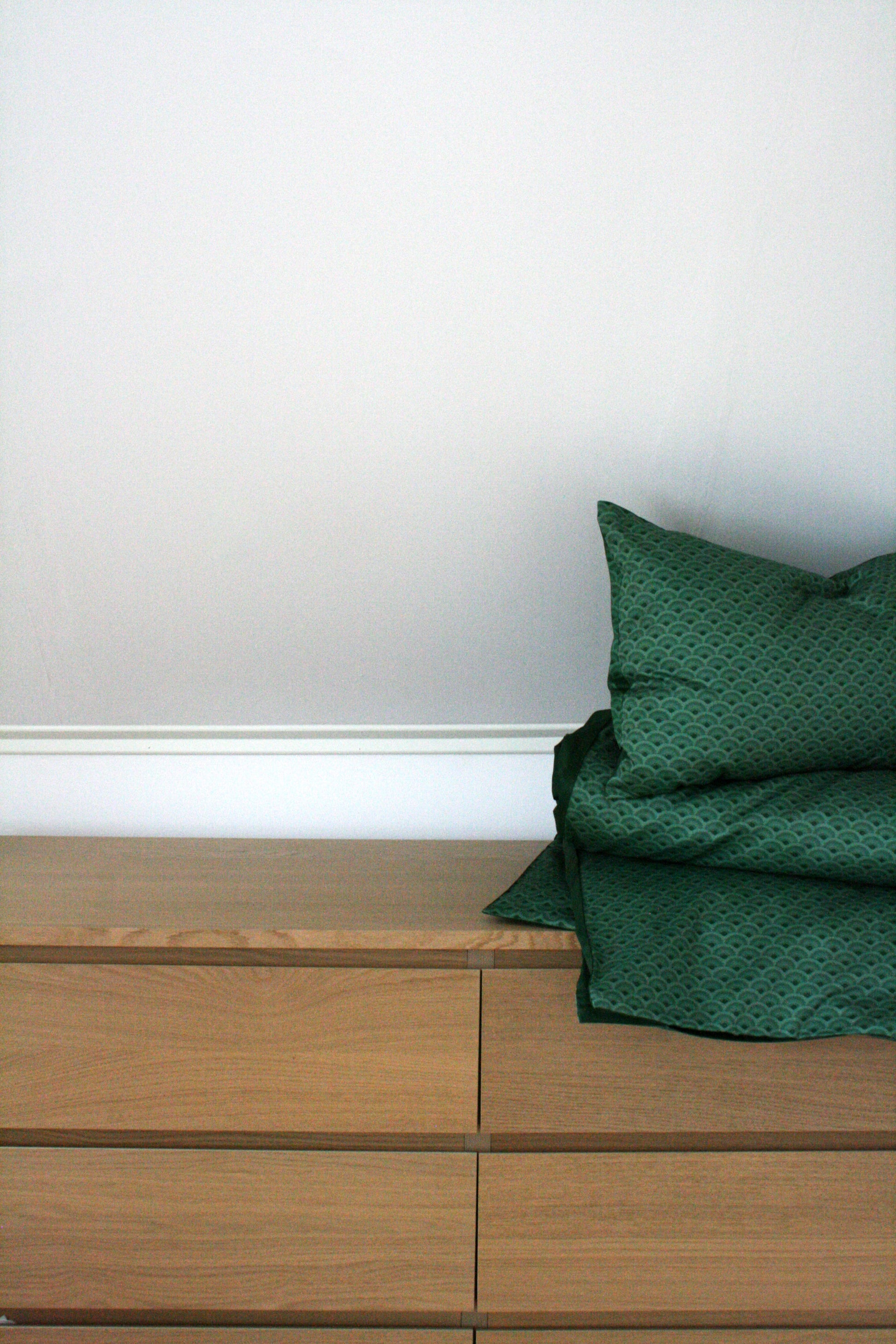 Påslakanset Vågor Bomullssatin Skogsgrön 210×150 cm, miljöbild. Vikta sängkläder på byrå,